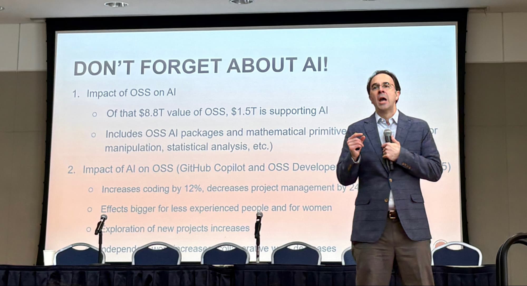 A man in a suit presents to a group of people in front of a screen.