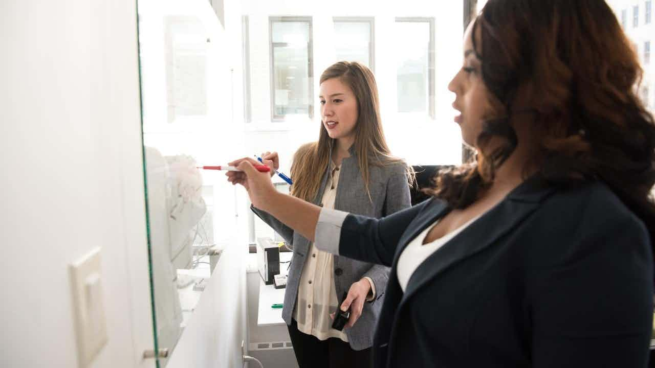 Two women work at a whiteboard. 