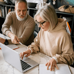 Two middle aged people, a white man and a white woman, use a laptop.