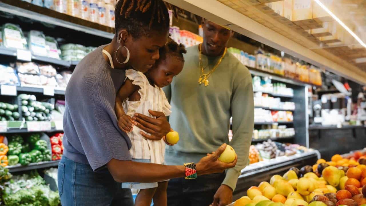 Two young parents and their baby look at fruit in the grocery store.