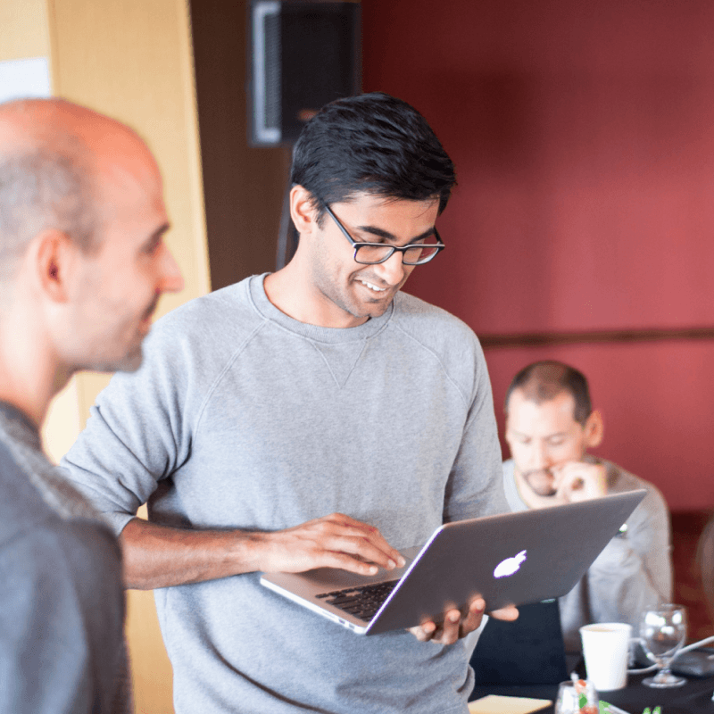 Nava CEO Rohan Bhobe stands with his laptop in an office alongside Nava employees.