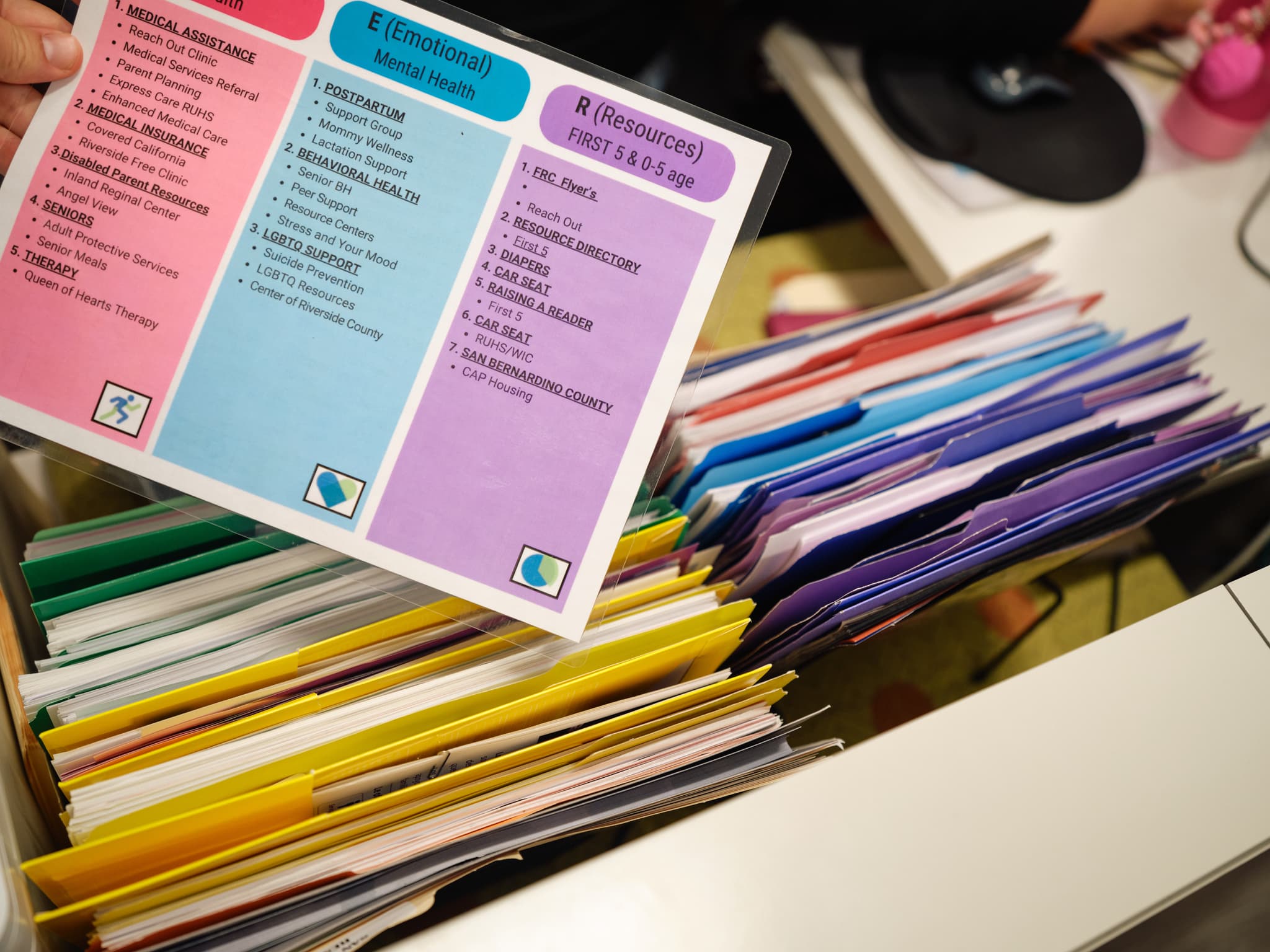 A staff member holds a resource guide that is color-coded in pink, blue, and purple.