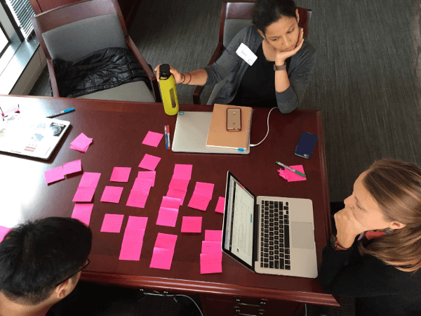 Two Navanauts are sitting at a table looking at a laptop computer and pink sticky notes.